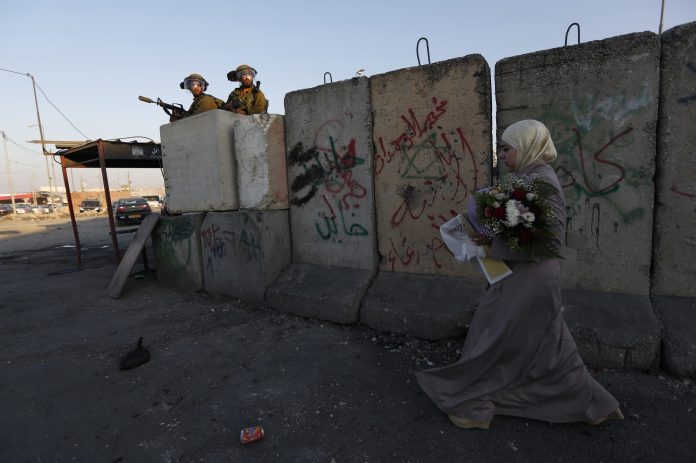 una mujer palestina pasea junto a soldados israelíes durante unas protestas contra la ofensiva israelí en Gaza, en Qalandia, cerca de la ciudad cisjordana de Ramala