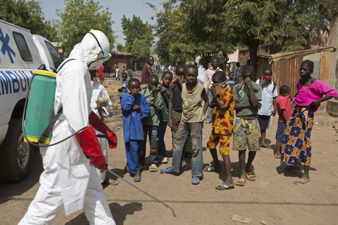 Niños observan mientras trabajadores de la salud esparcen desinfectante en las afueras de una mezquita en Bamako