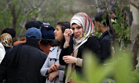 Headscarfed women wipe away tears as they stand together at funeral